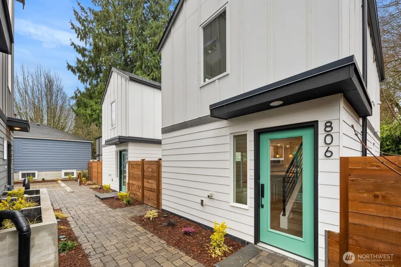 Two completed white detached cottages with teal entry doors and a paver walkway between them